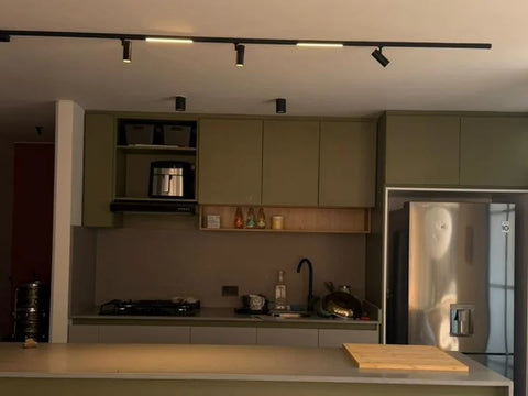 Cocina real con muebles verde oliva iluminada con riel de spots LED negro sobre la isla y la barra